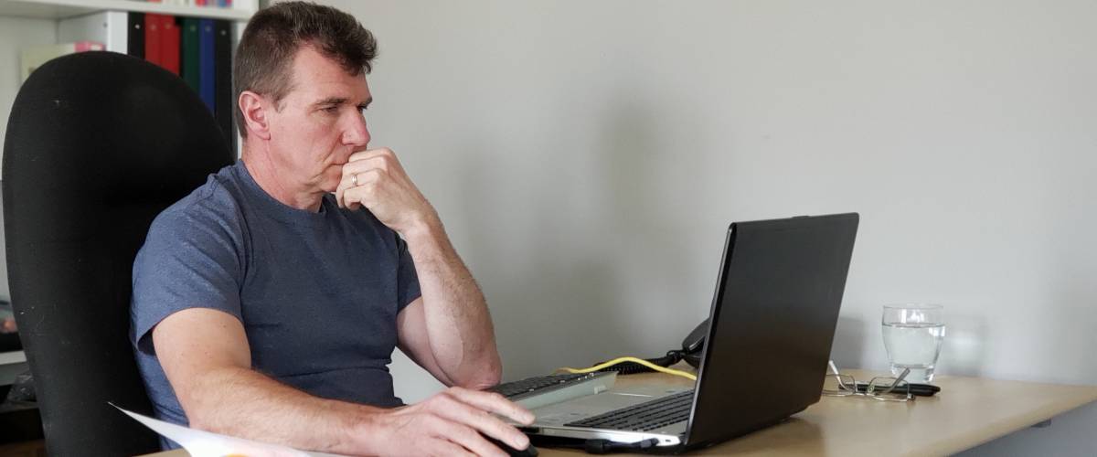 Man sits in home office, looking at laptop.