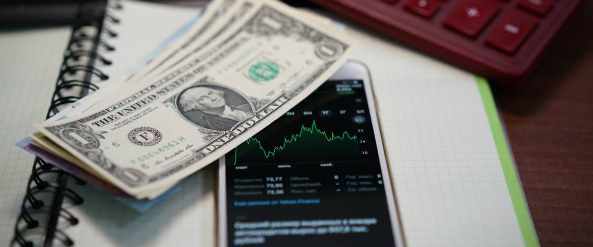 American dollar bills against phone displaying stock trends