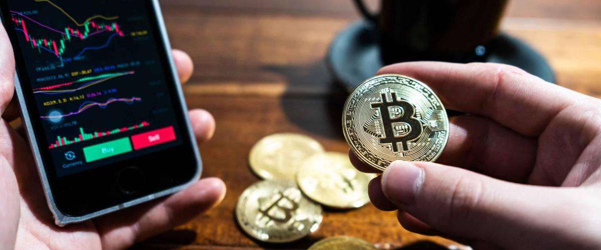 Smartphone with Bitcoin trading chart on the screen. Holding in hand a gold Bitcoin Cash coin. Trading on the cryptocurrency exchange.