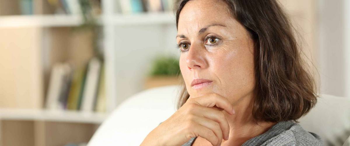 Pensive adult woman looking away sitting in the sofa in the living room at home