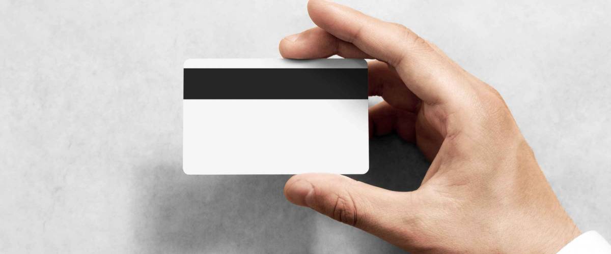 Hand holding blank white credit card mockup with black magnetic stripe, back side view. Plastic bank-card design mock up with magstripe.