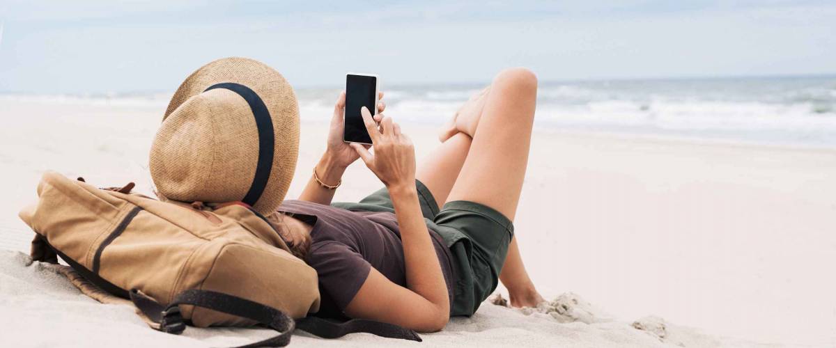 Young woman lying with smart phone on a beach. Girl looking at mobile phone. Relaxation, connection, social distance, mobile apps, rest, vacations, holidays, online shopping concept