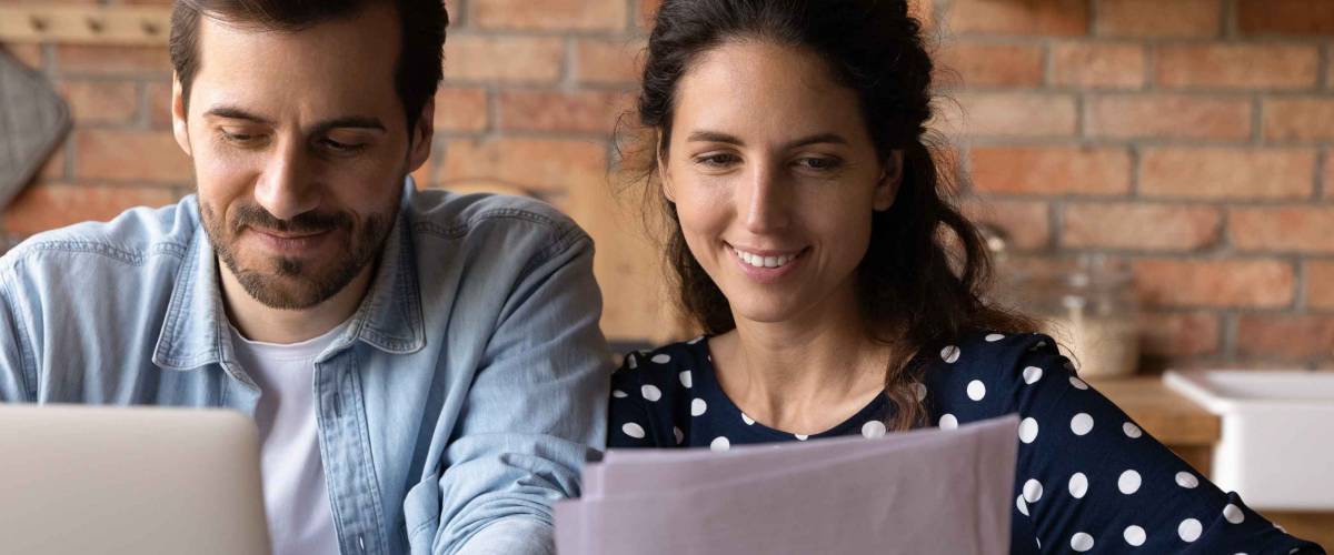 Happy young married couple reviewing loan, mortgage agreement, analyzing fee schedule, planning costs and family budget. Husband and wife using laptop and reading documents together