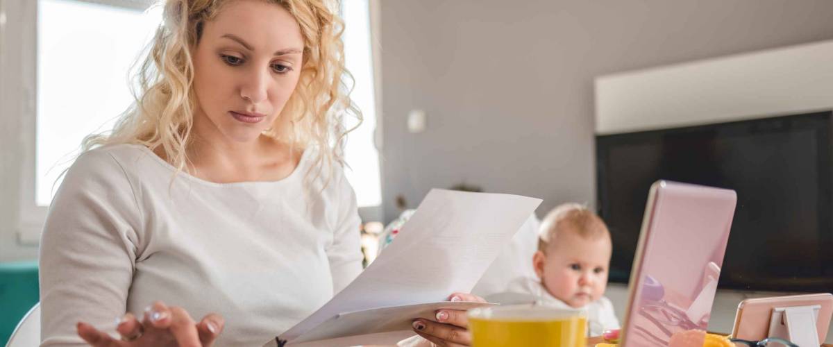 Mother holding letter and using calculator at home office and taking care of her baby