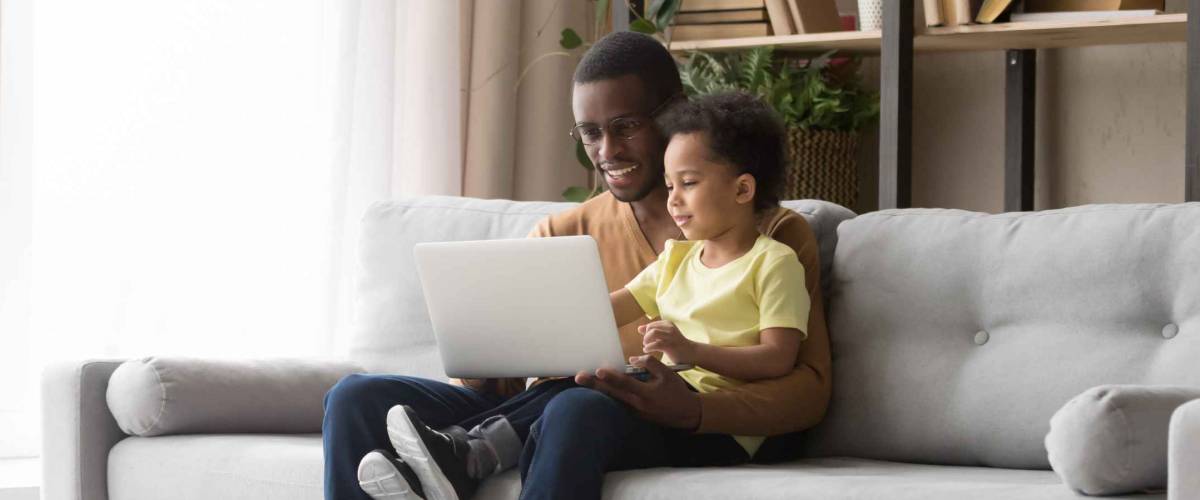 Young father and son using laptop at home on couch.