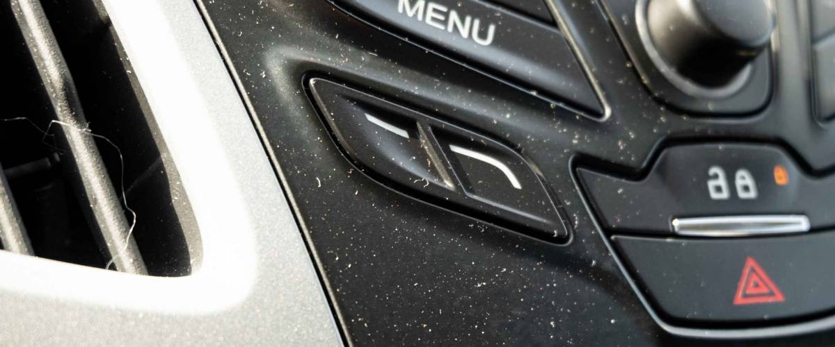 The interior dashboard of a car is building up dust, dirt, and debris.