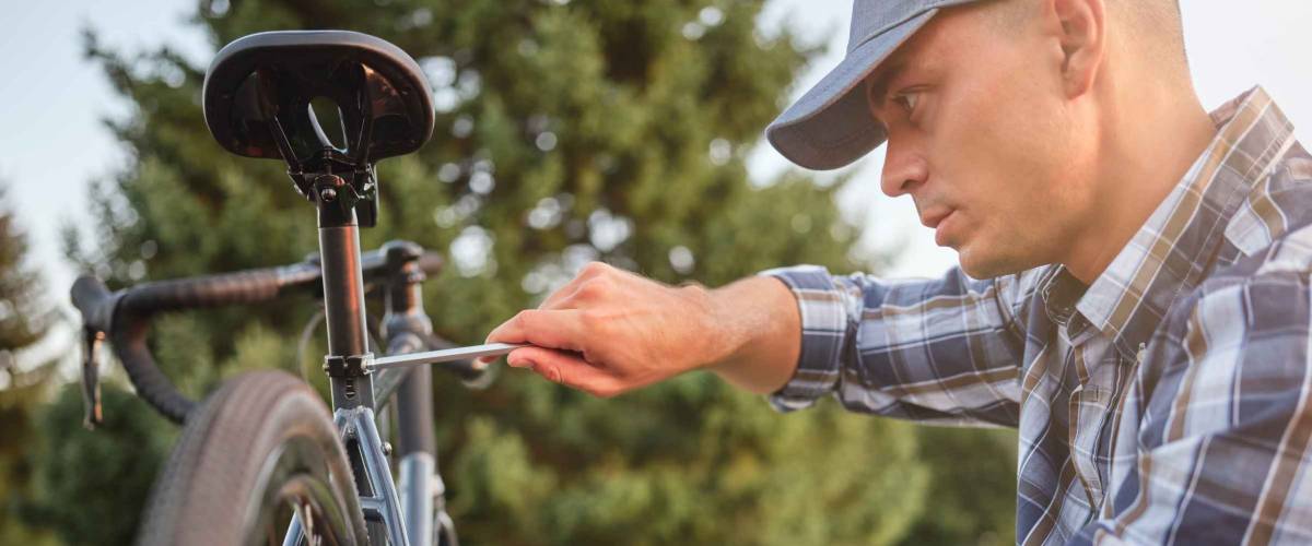 It needs to be fixed. Side view of concentrated young caucasian man in casual wear using a screwdriver while repairing his bike in the public park