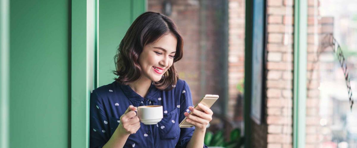 Beautiful cute asian young businesswoman in the cafe, using mobile phone and drinking coffee smiling