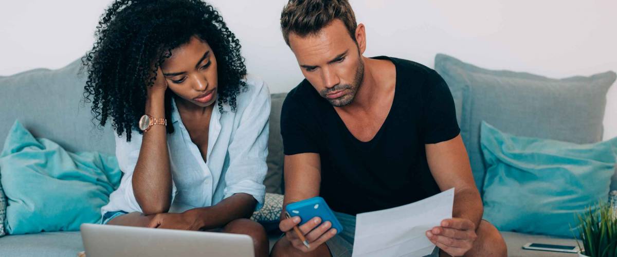 Young interracial couple in the couch stressed with financial problems doing calculations with paper work