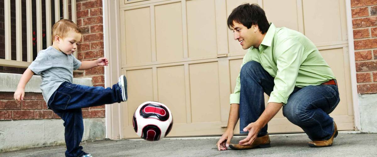 Father teaching son to play soccer on driveway