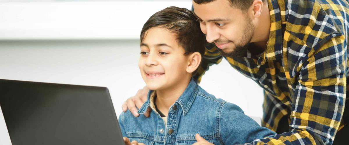 Study online. Cheerful young African man smiling helping his cute young son on a laptop computer.