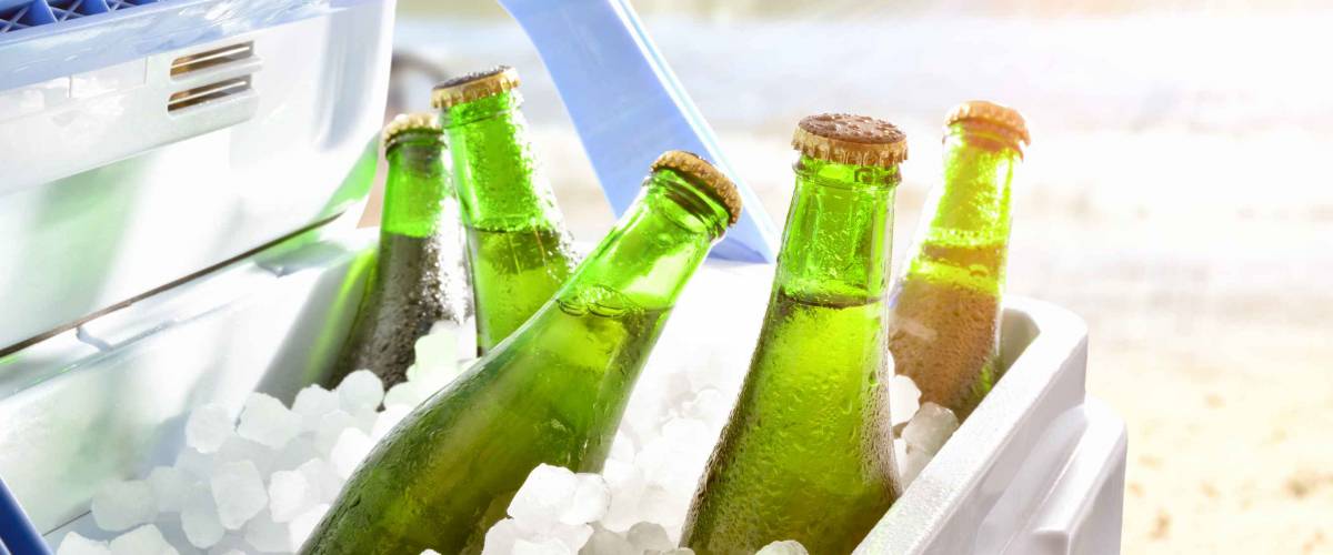 Bottles of beer chilled on ice in a camping fridge on a beach on a hot day with sunshine.