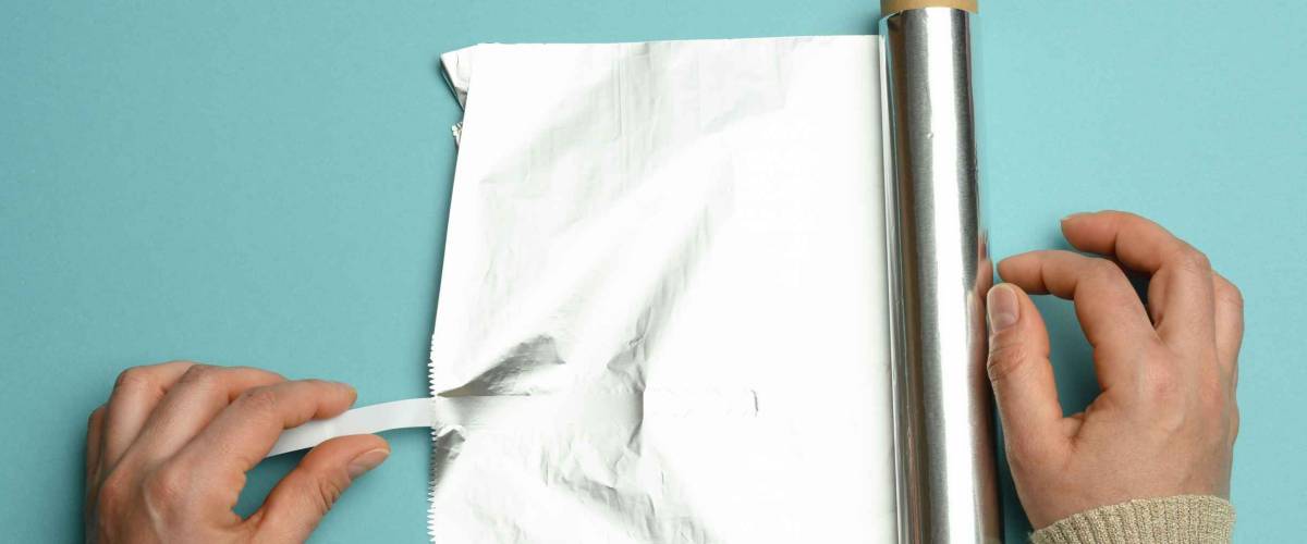 female hand holds an unfolded roll of gray foil on a blue background, close up