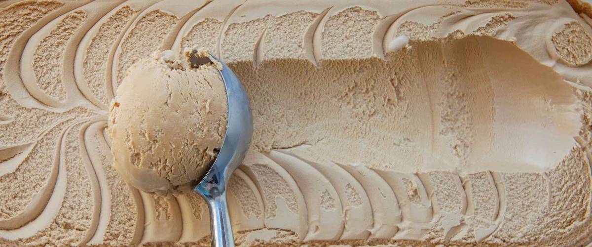 Creme brulee ice cream Flat lay. Top view. Spoon for ice cream takes a little out of the package. Macking ball of ice cream. Space for text.