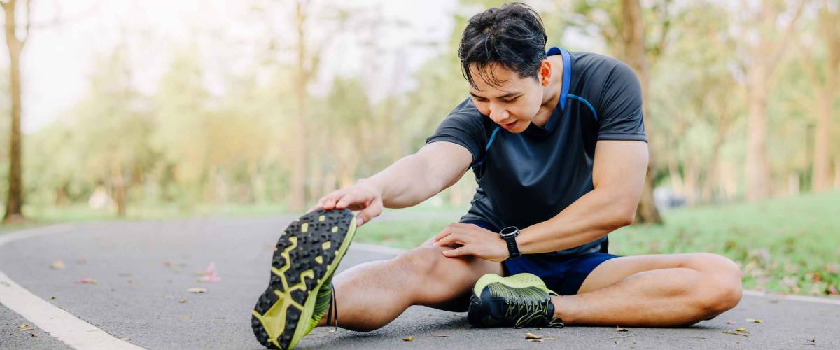 Close up shot of athlete runner young Asian male stretching his leg on race track in the park