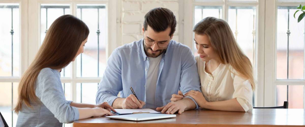 Happy young clients signing paper contract with professional