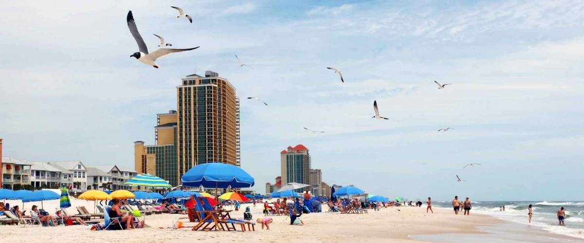 Alabama Gulf of Mexico beach life. Marine landscape with beach line homes and hotels, beach umbrellas, people and flying birds on a foreground. Alabama Gulf Shores State park and beach, USA.