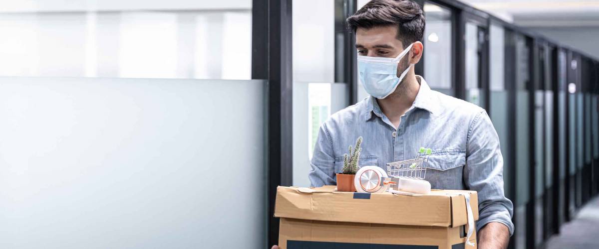 Man leaving office wearing a mask and holding a box with belongings in it.