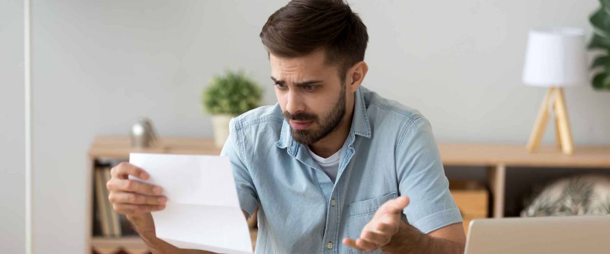 Confused frustrated young man holding letter looking shocked.