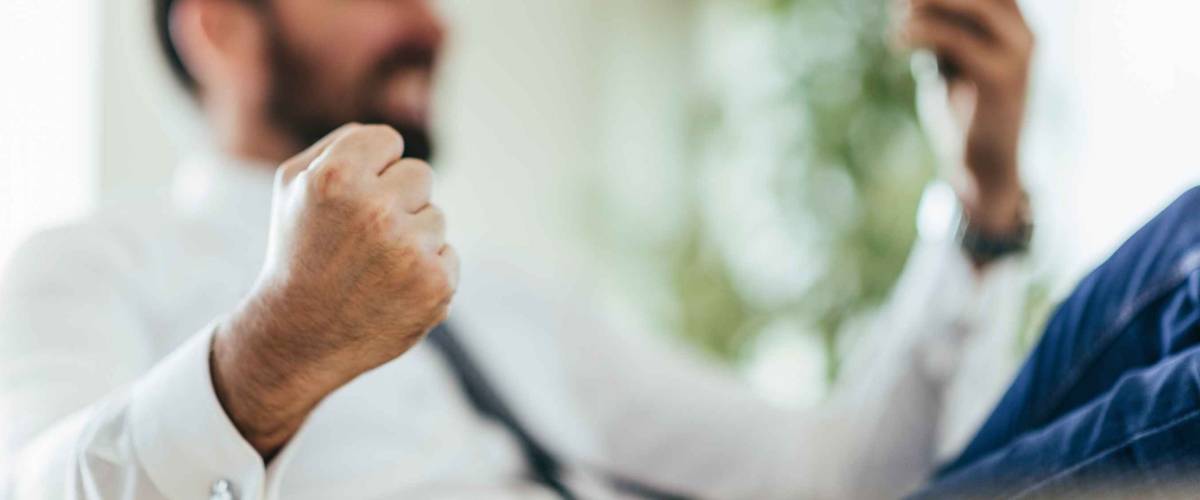 Businessman getting good news over smart phone, fist pumping. Selective focus on fist
