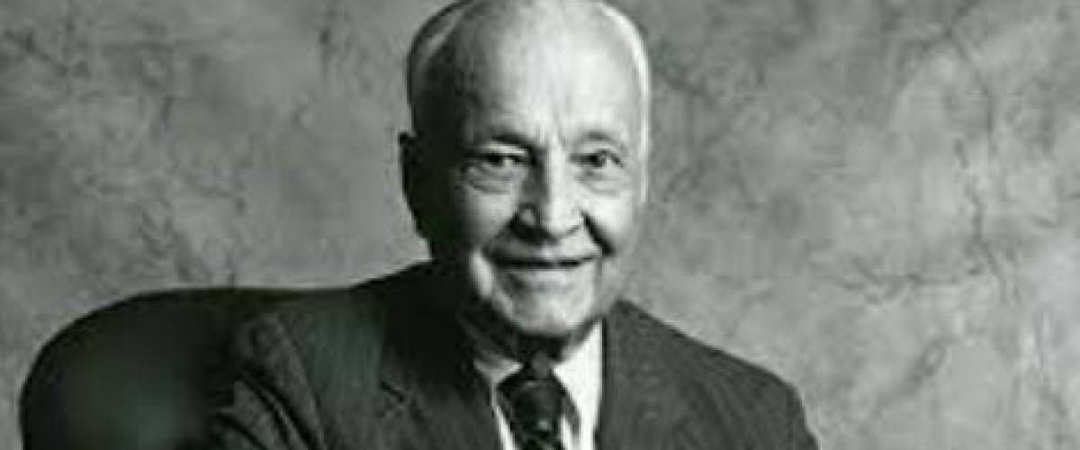 Sir John Templeton poses for the camera, sitting at a desk, smiling.