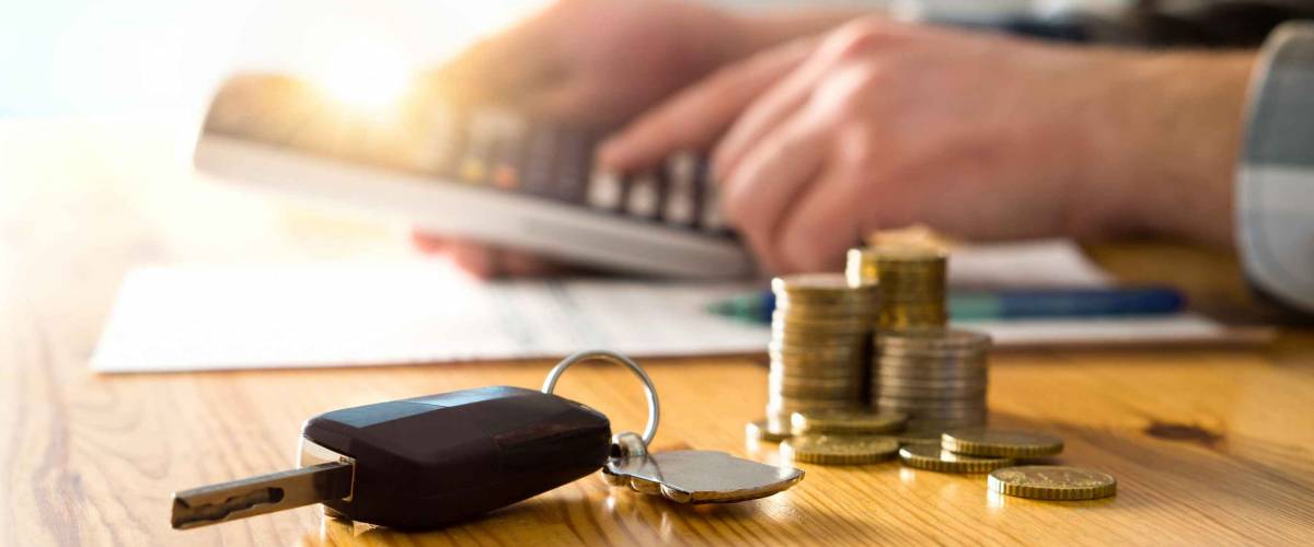Car keys and money on table with man using calculator.