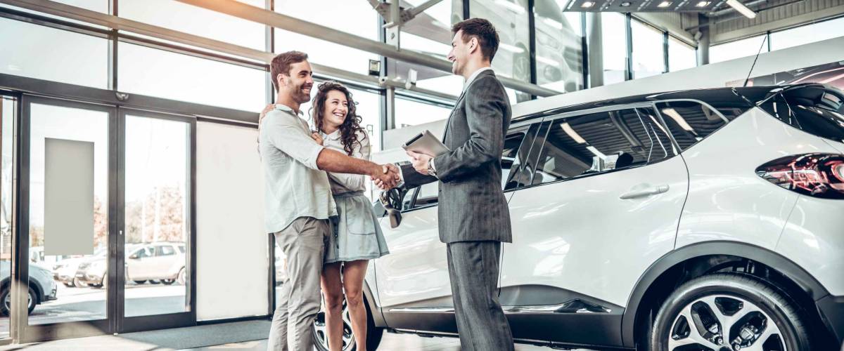 Young couple shaking hands with sales agent after a successful car buying.