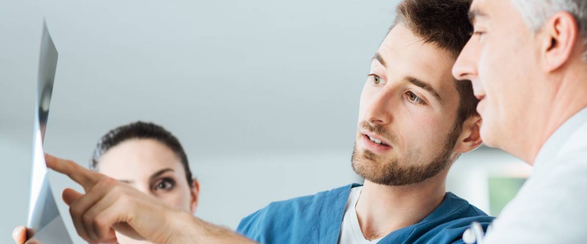 Professional medical team with doctors and surgeon examining patient's x-ray image, discussing and pointing