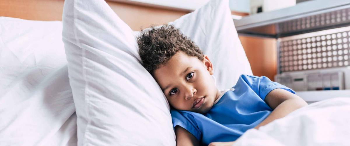 little african american boy with drop counter lying in bed in clinic