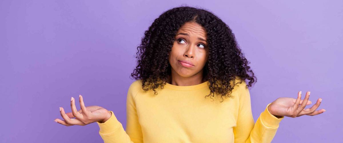 Photo of puzzled cute dark skin girl dressed yellow sweatshirt shrugging shoulders looking empty space isolated purple color background