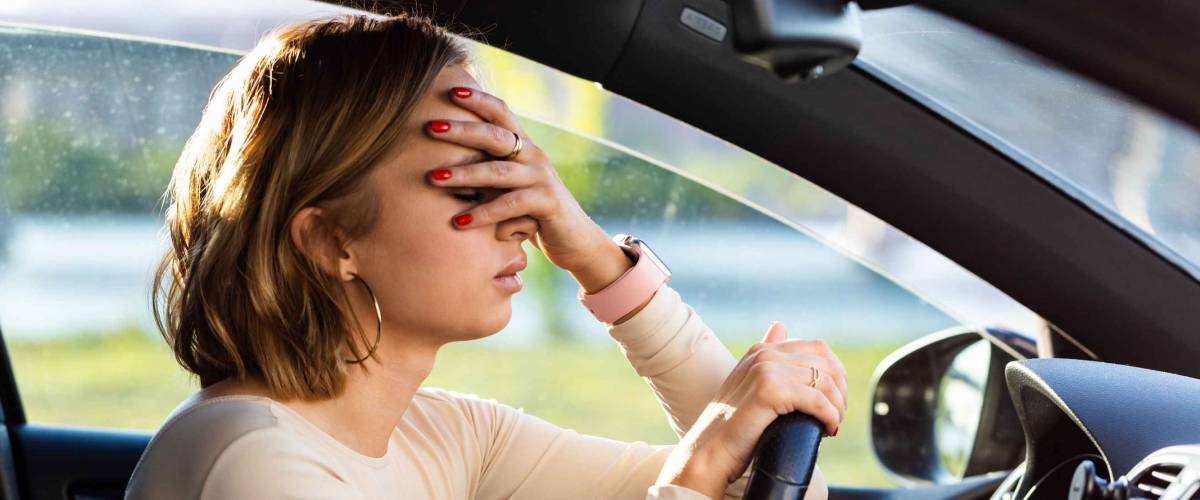Exhausted woman driver feeling headache, sitting inside her car, keeping hand to head and feeling anxiety. Stop after driving car in traffic jam.Blood pressure
