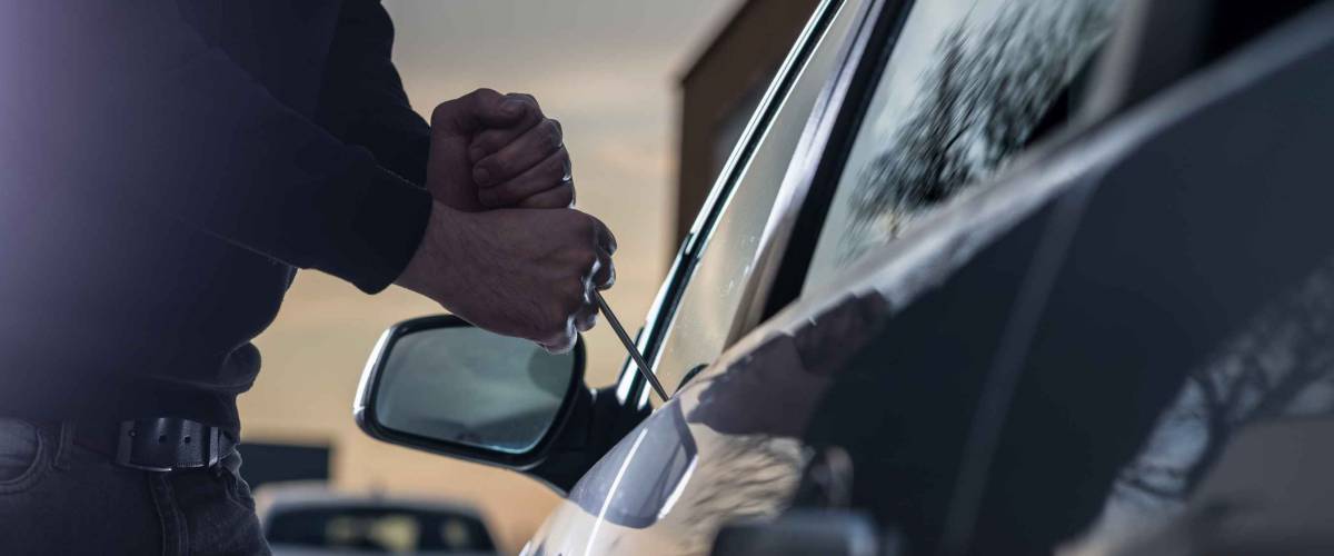 Auto thief in black balaclava trying to break into car with screwdriver. Car thief, car theft