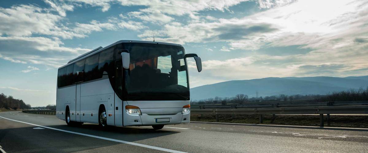 White Modern comfortable tourist bus driving through highway at bright sunny sunset. Travel and coach tourism concept. Trip and journey by vehicle