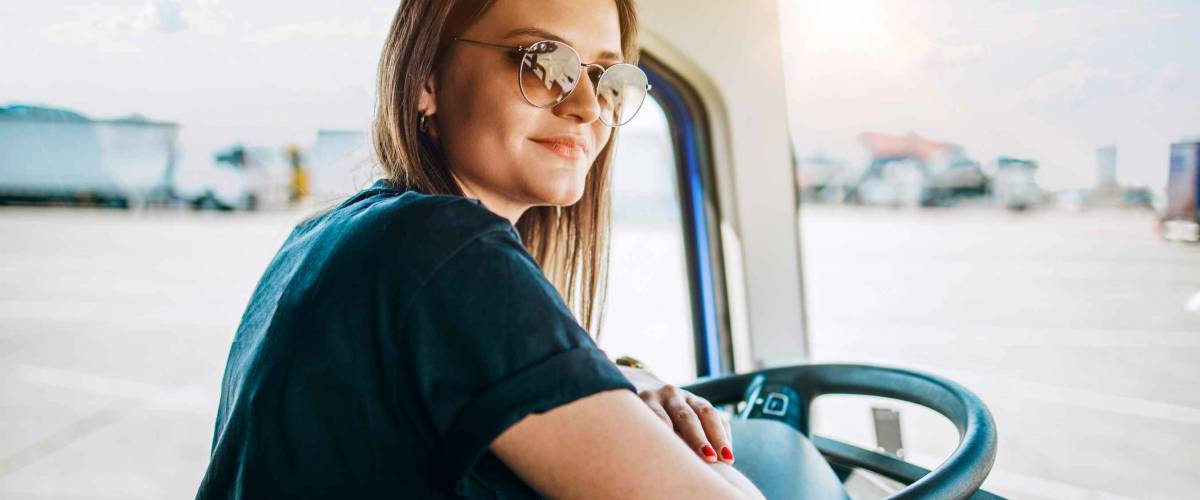 Portrait of beautiful young woman professional truck driver sitting and driving big truck. Inside of vehicle. People and transportation concept.