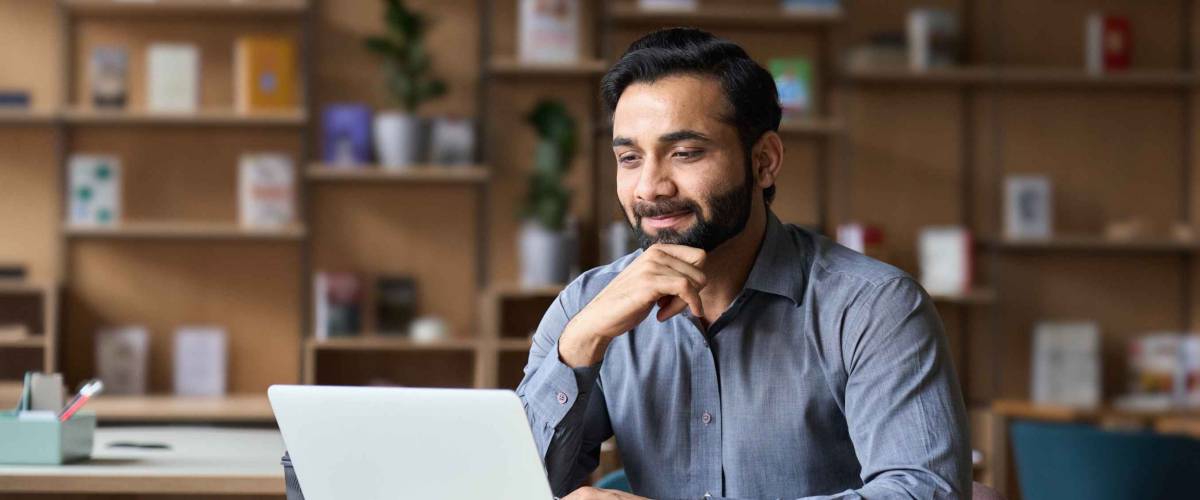 Smiling man working on laptop in modern office lobby space.