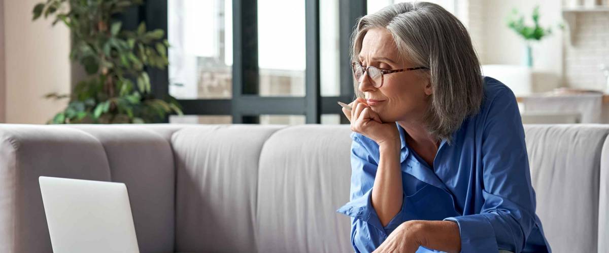 Senior mature older woman looking at laptop while sitting at a desk.