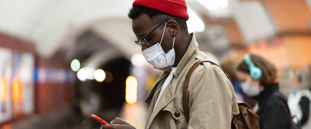 Afro-American millennial man in trench coat, red hat wearing face mask