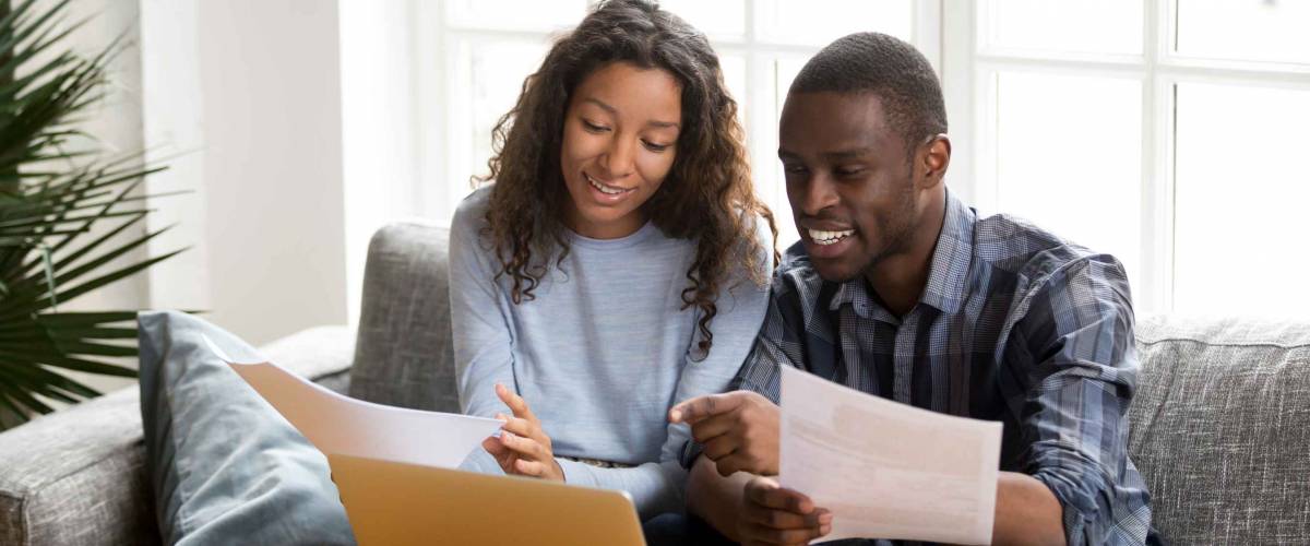 African black positive married couple sitting on sofa at home looking for a low mortgage rate.