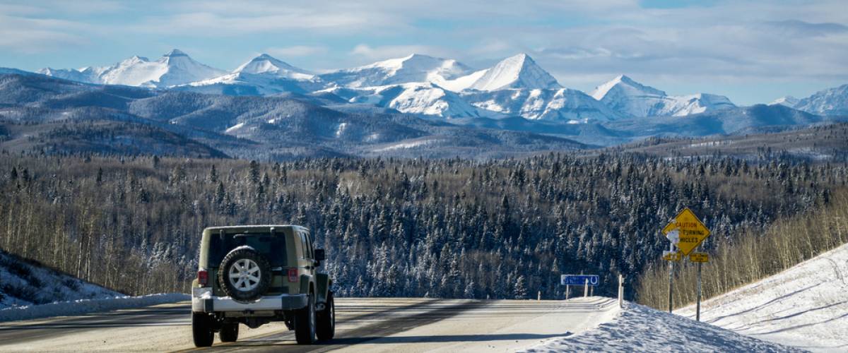 A Jeep driving down a road toward a snowcapped mountain range