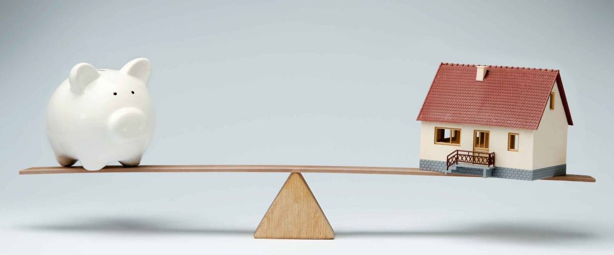 Home loans market. Model house and piggy bank balancing on a seesaw