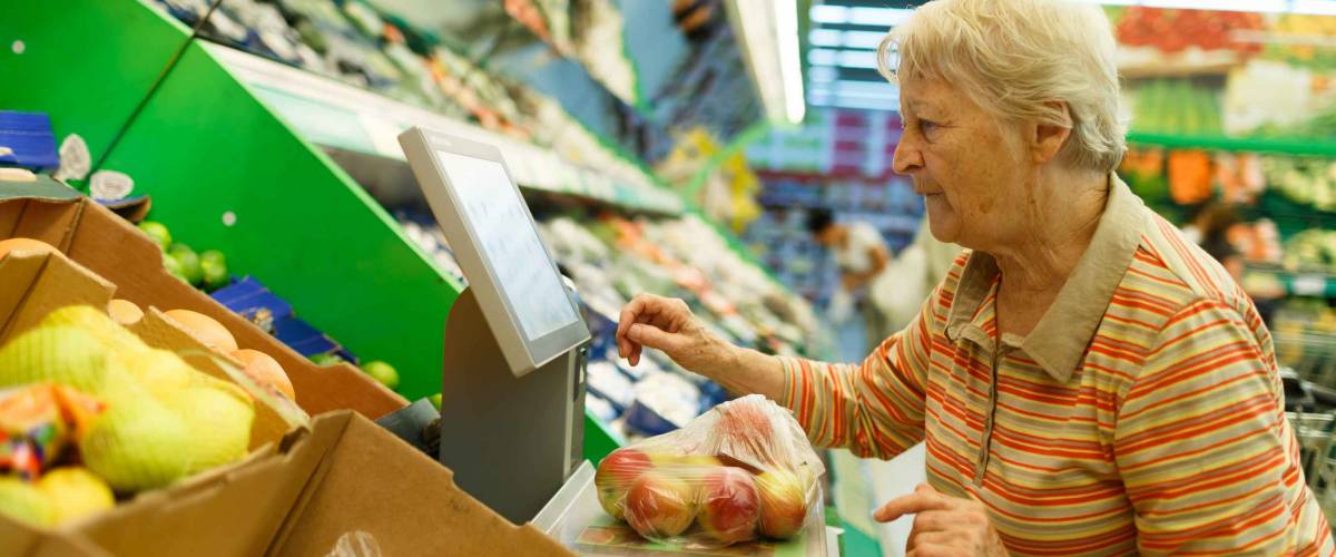 Elderly woman weighing goods on digital weight in supermarket, shopping for fruits and vegetables in produce department of a grocery store/supermarket (color toned image)