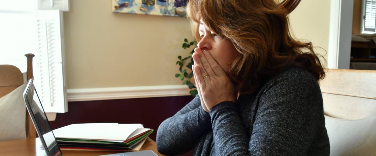 A woman looks frustrated and holds her hands to her mouth while doing bills on her computer
