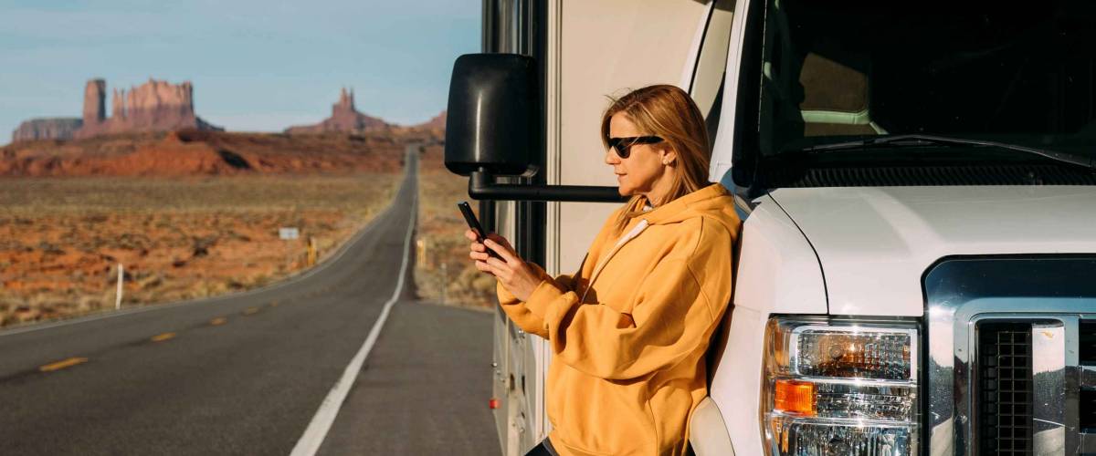 A woman travels by motorhome through Monument Valley in the USA desert and checks her mobile phone parked on the side of the road