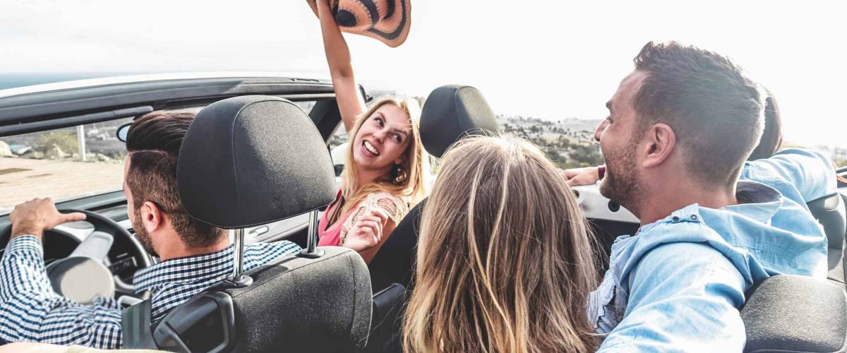 Happy friends with hands up having fun in convertible car
