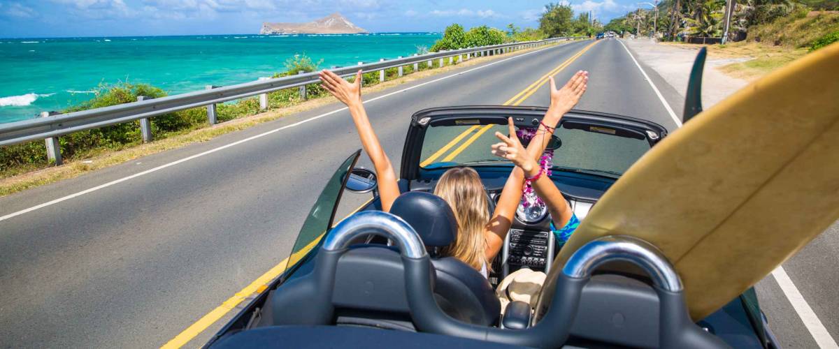 Road trip travel - girls driving car in freedom. Happy young girls cheering in convertible car on summer Hawaii vacations.