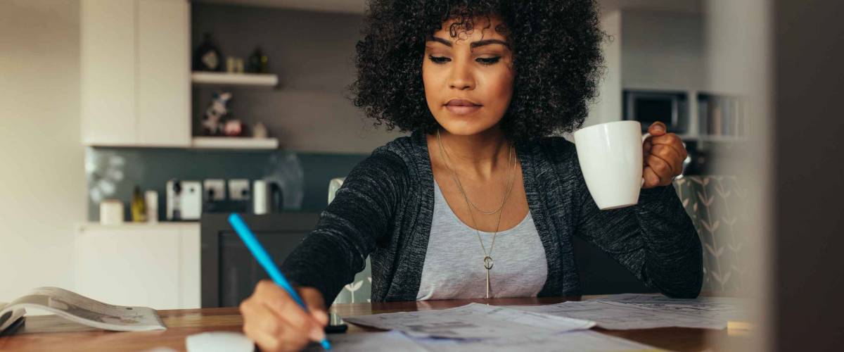 Female architect making a project plan with cup of coffee in hand. Interior designer correcting a drawing while sitting at home office.