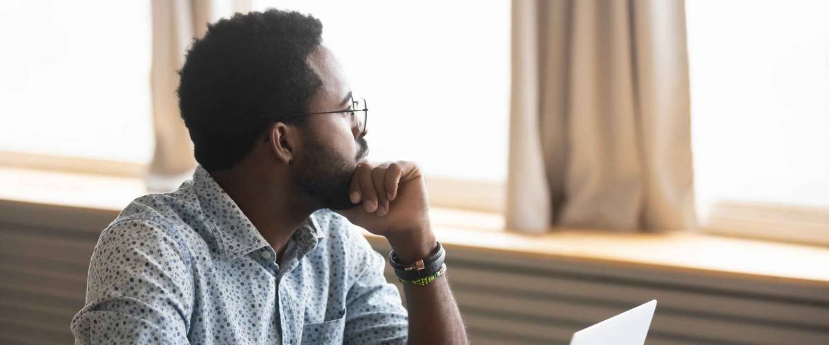 Thoughtful african American male employee in glasses sit at desk distracted from computer work pondering, pensive biracial man look in distance thinking or planning, business vision concept