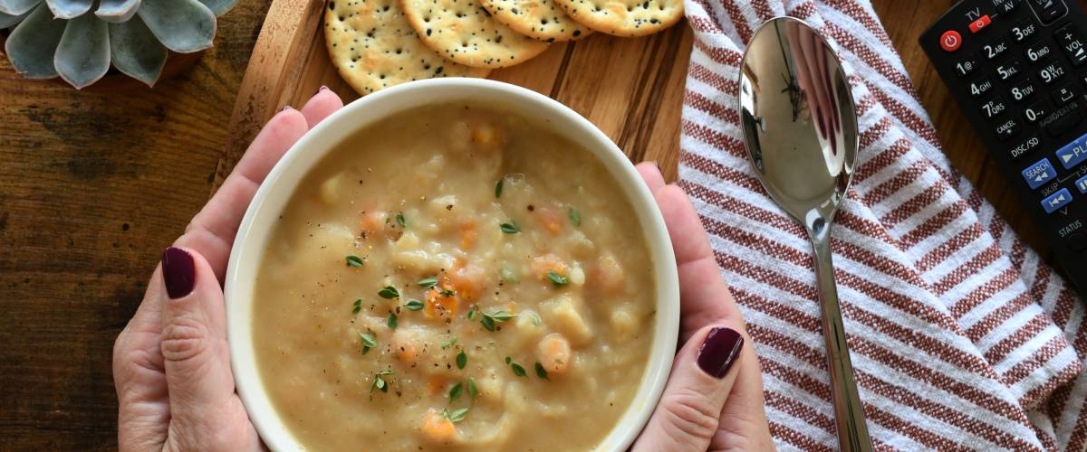 Woman putting a bowl of potato soup on a tray with crackers & TV remote for cozy night in.