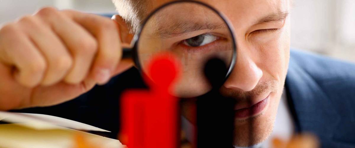 Man in suit look thru loupe on statuettes closeup in office. How to find a recruiter.