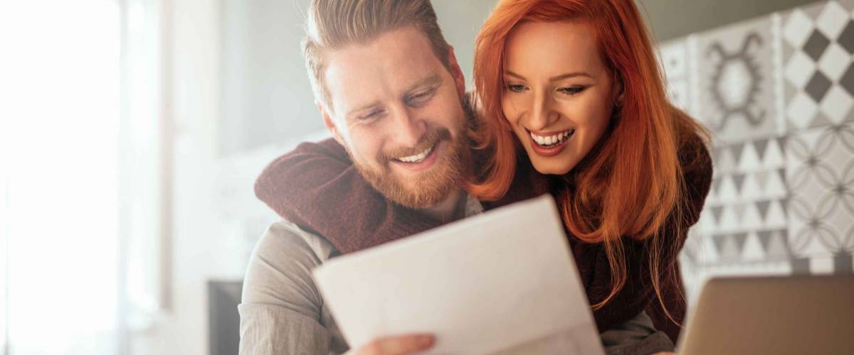 Photo of a positive young couple embracing and calculating the bills at home.